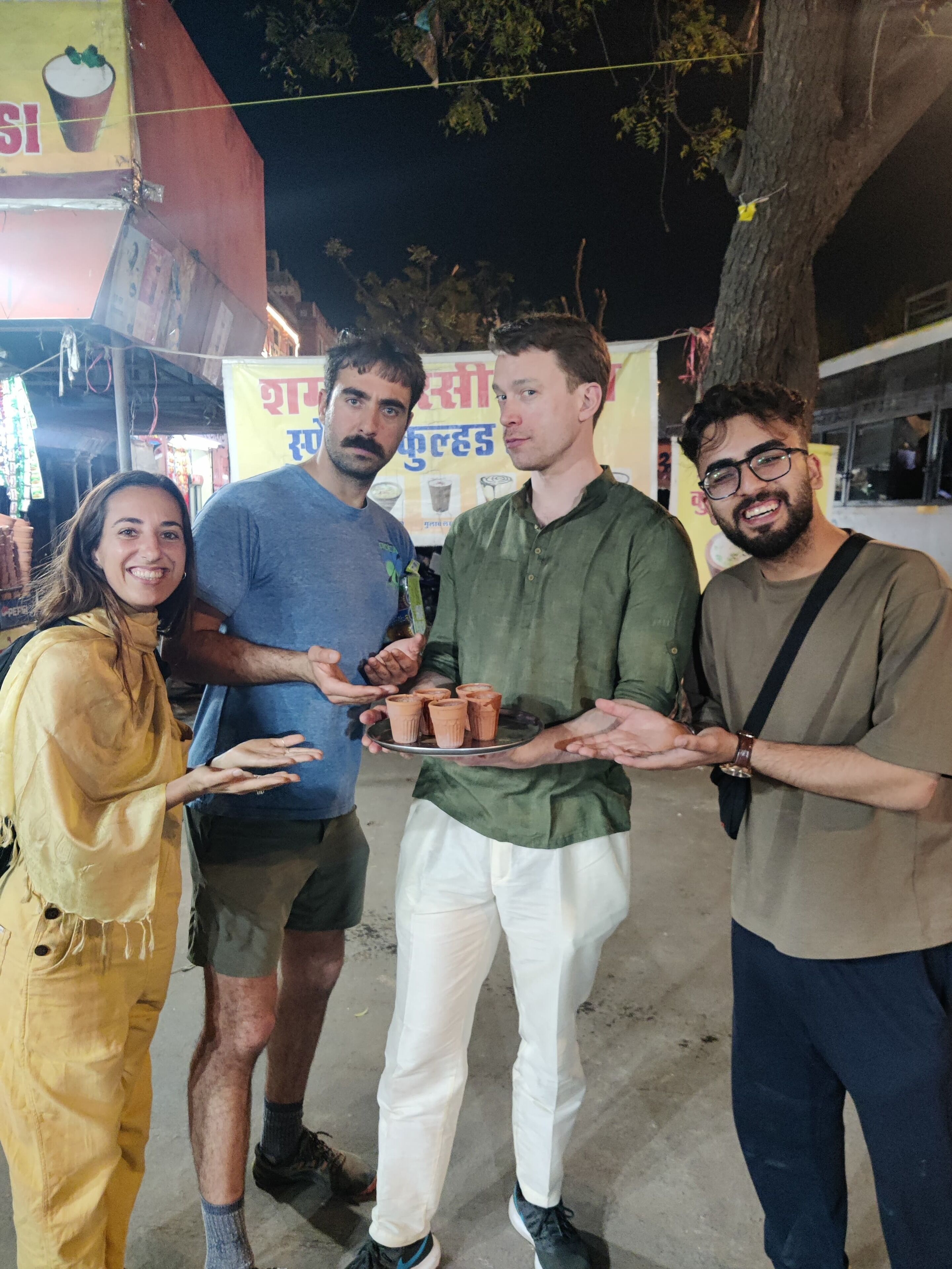 A group of people standing outdoors at night, holding a tray with small clay cups.