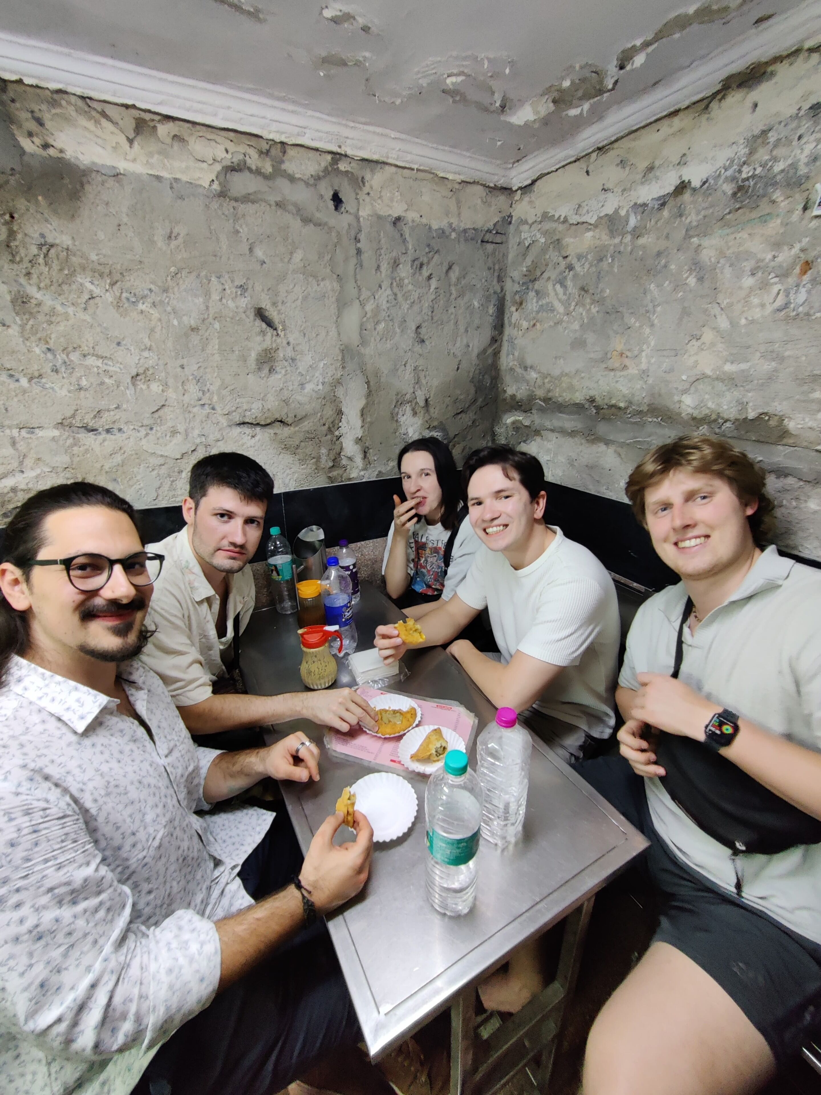 Un grupo de personas sentadas alrededor de una mesa en una habitación con una pared rugosa y con textura.