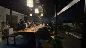 Un grupo de personas sentadas alrededor de una mesa de madera en una habitación con poca luz y lámparas colgantes.