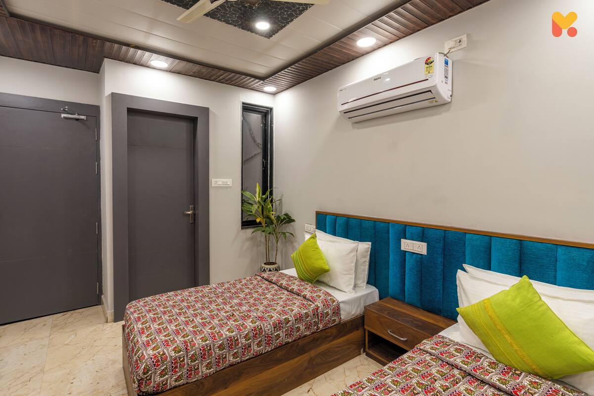 Une chambre d’hôtel avec deux lits, une tête de lit en bois, une plante en pot et un appareil de climatisation.
