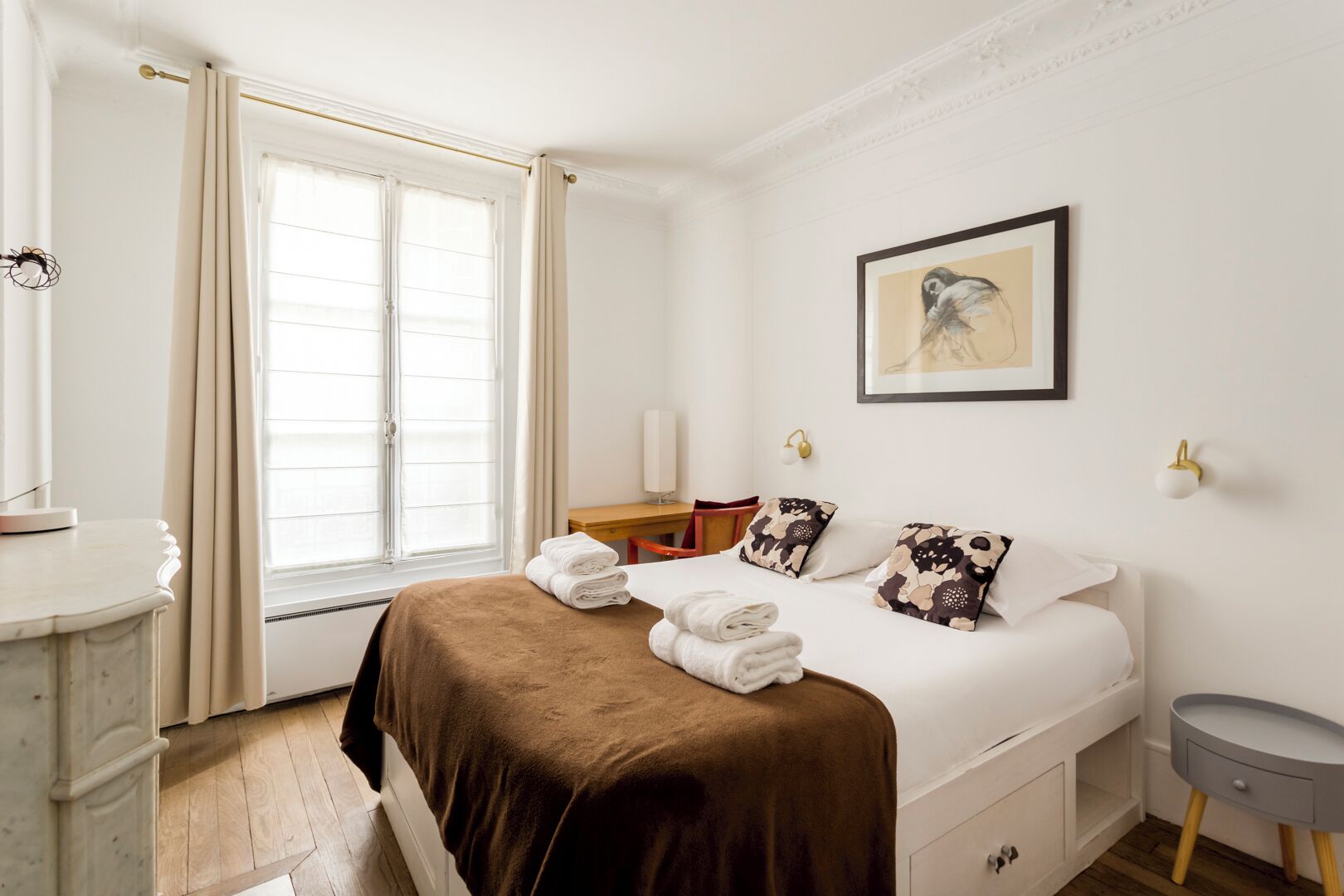 A hotel room with a bed, a desk, a chair, a bedside table, and a window with curtains.