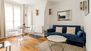 En moderne stue med en blå sofa, et glasbord og transparente stole.