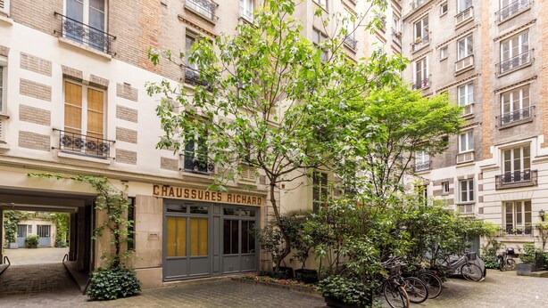 A building with a sign reading "CHAUSSURES RICHARD" and a courtyard with a tree and bicycles.