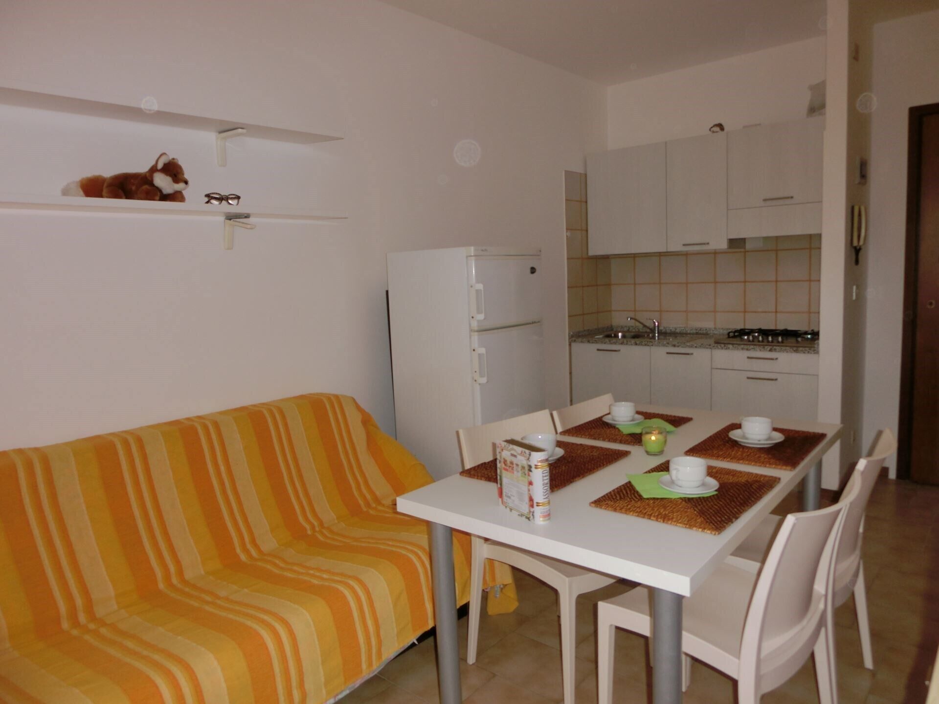 Un espace de vie compact comprenant un canapé à rayures, une table à manger avec des chaises, un réfrigérateur et un coin cuisine.