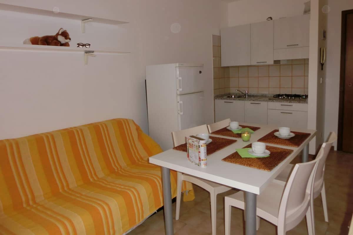 A compact living space with a striped sofa, a dining table with chairs, a refrigerator, and a kitchenette with cabinets and a stove.