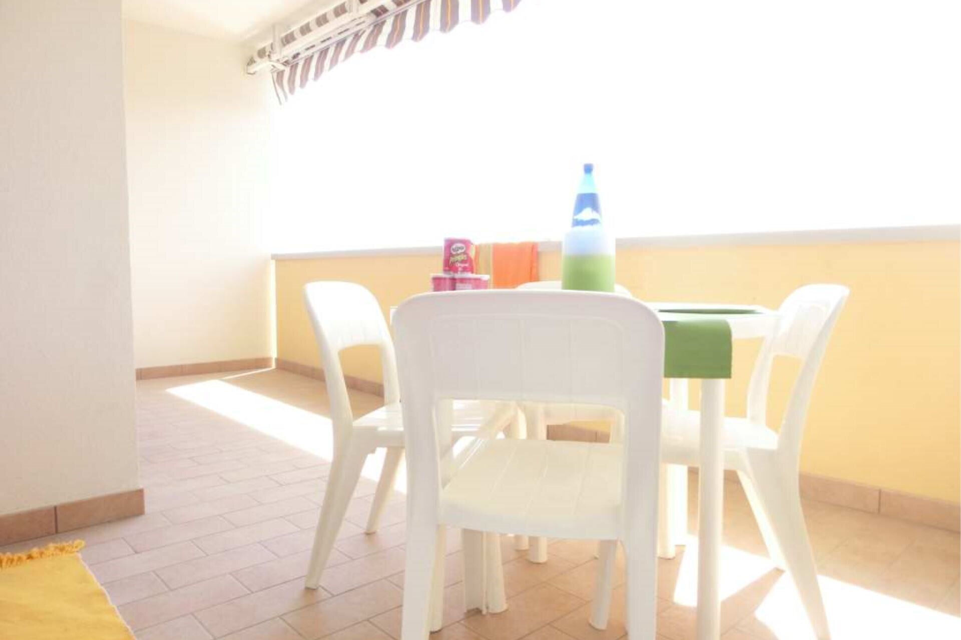 Ein kleiner Balkon mit Tisch und Stühlen, einer Wasserflasche und einer kleinen Packung Taschentücher.