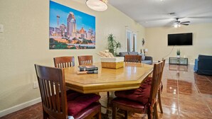 A dining area with a wooden table, chairs, a chandelier, a cityscape painting, a television, and a ceiling fan. - ~Bamboo Oasis Relaxing Hot Tub Family Time~ Get to Anywhere in SA in 20 mins! (San Antonio)