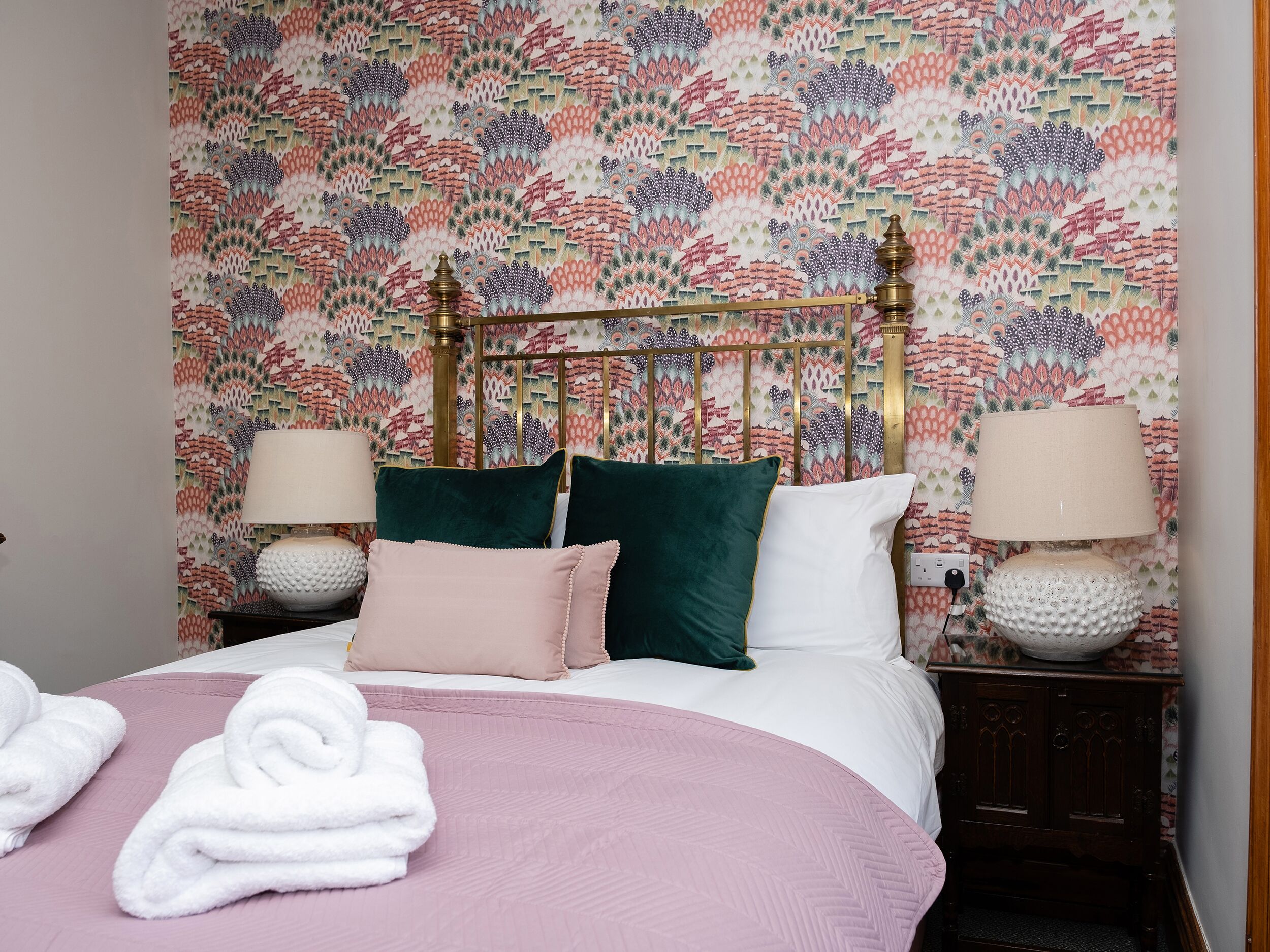 A neatly made bed with a pink bedspread, two pillows, and two bedside lamps.