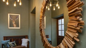 A room with a wooden bench, a large mirror, and a light fixture with exposed bulbs. - Watermouth Castle, Rhododendron Apartment (Ilfracombe)
