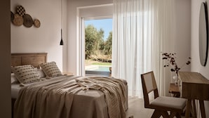 Ein Schlafzimmer mit Bett, Schreibtisch und Stuhl. Es gibt ein Fenster mit Vorhängen und Blick auf Bäume sowie einen Pool.