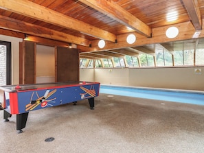 Een pool tafel in een ruimte met houten balken, een zwembad en een raam met uitzicht op bomen.