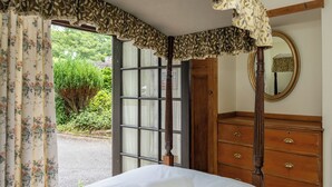 Ein Schlafzimmer mit einem Bett, einer Holzkommode, einem Spiegel und einem Fenster mit Vorhängen.