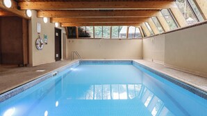 Una piscina interna con travi in legno, un salvagente e un cartello di sicurezza.