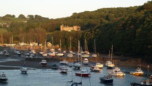 Un porto con numerose imbarcazioni ormeggiate, un castello su una collina e un paesaggio verdeggiante.