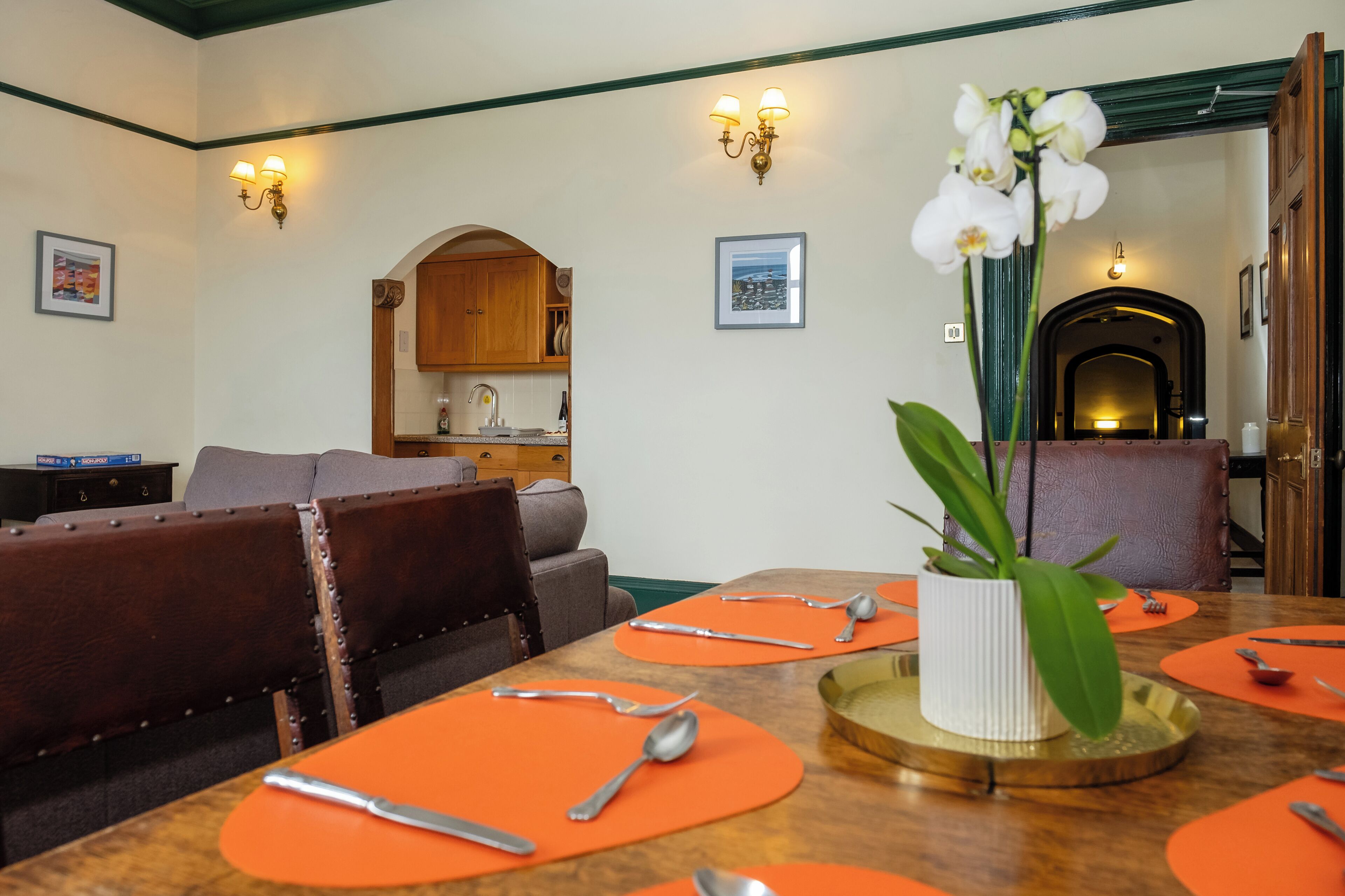 Ein Essbereich mit einem Holztisch, gedeckt für vier Personen, orangefarbenen Platzsets und einer Topf-Orchidee.