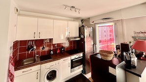 A compact kitchen with white cabinets, a stainless steel refrigerator, a washing machine, and a coffee maker. - Beautiful 65 m² flat (Saint-Raphaël)