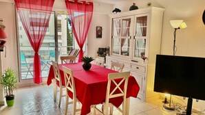 A dining area with a red tablecloth, white chairs, a TV, and a cabinet. - Beautiful 65 m² flat (Saint-Raphaël)