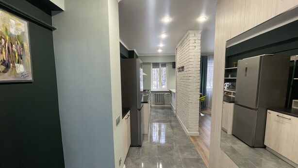 A modern kitchen with stainless steel appliances, a tiled floor, and a view into the adjacent living area. - NicePlace in the Old Center Almaty (Almaty)