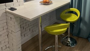A modern kitchen with a white brick wall, a hanging pendant light, a window with decorative iron bars, and a fruit basket on the counter. - NicePlace in the Old Center Almaty (Almaty)