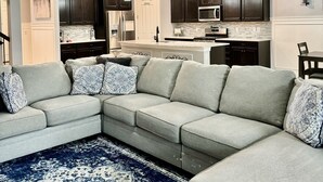 Ein modernes Wohnzimmer mit einem Ecksofa, einem gemusterten Teppich und einem Deckenventilator.