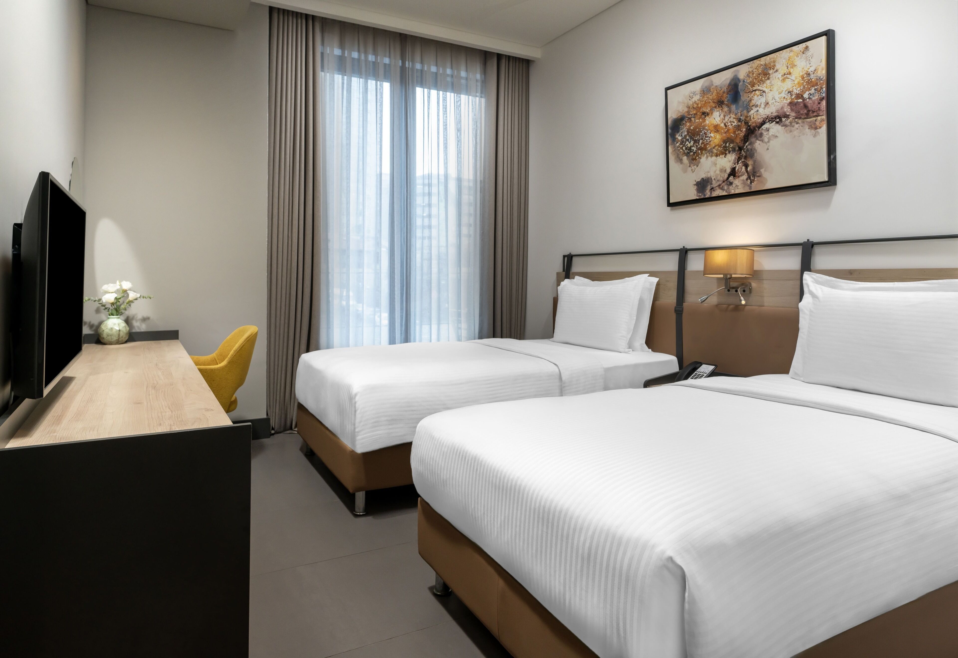 Ein Hotelzimmer mit zwei Betten, einem Schreibtisch, einem Fernseher, einer Lampe und einem Bild an der Wand.
