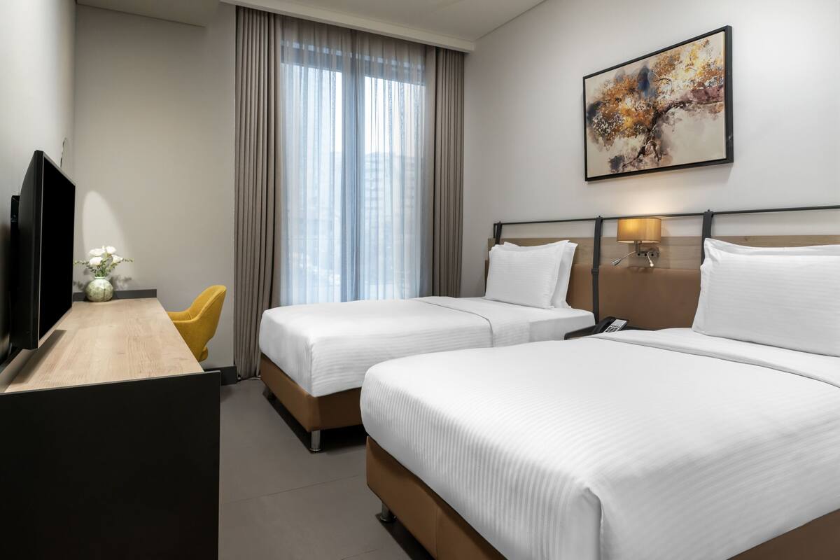 A hotel room with two beds, a desk, a TV, a lamp, and a painting on the wall.
