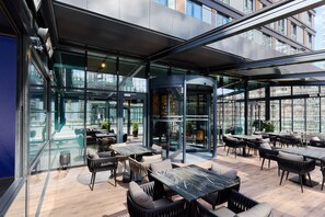 A modern outdoor seating area with glass walls, tables, and chairs. - Bomonti Suites (Istanbul)