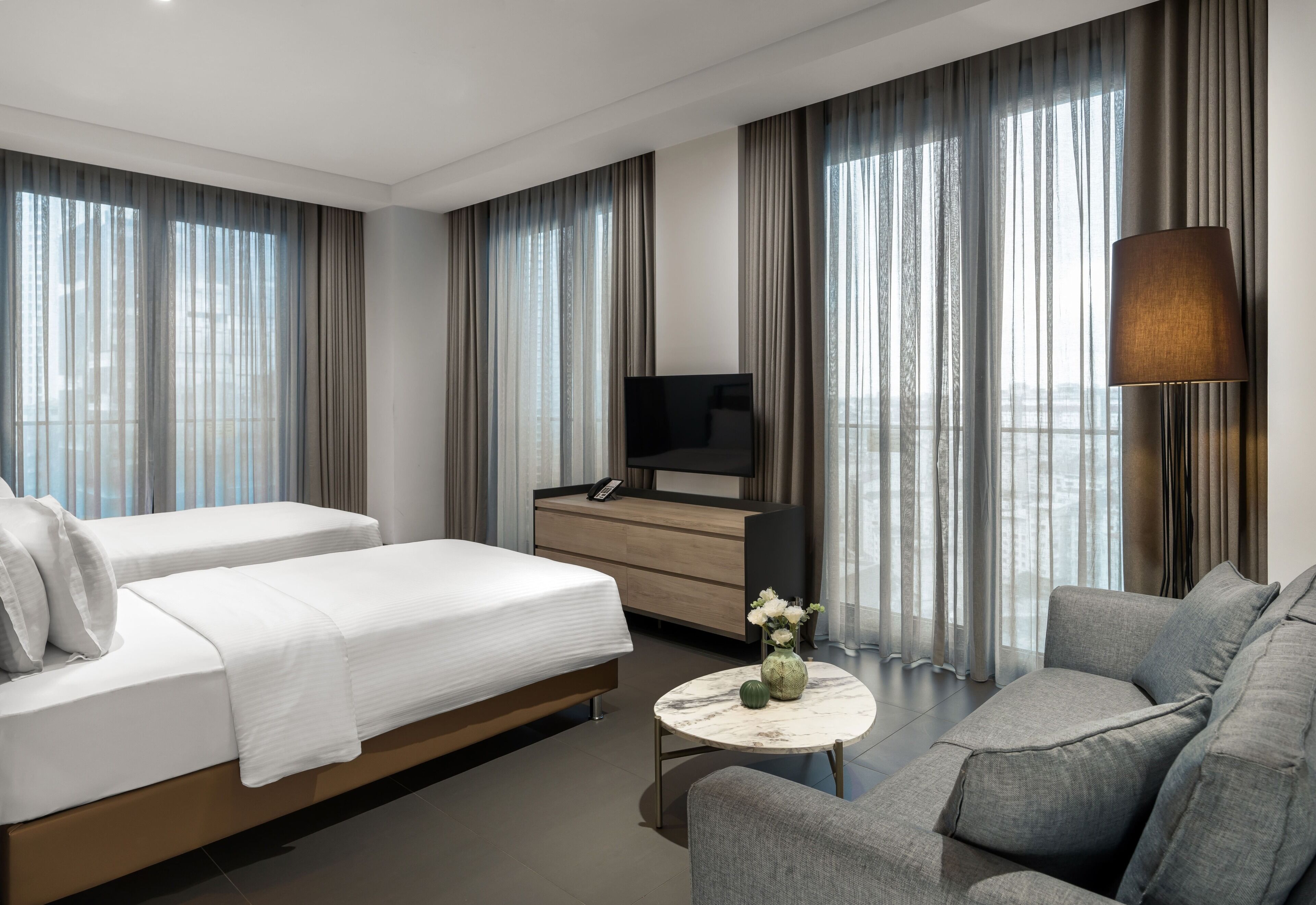 A hotel room with two beds, a sofa, a TV, a desk, and a lamp.