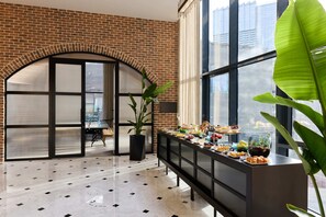 A modern interior with a brick wall, a large arched doorway, a buffet table with various food items, and a potted plant. - Bomonti Suites (Istanbul)