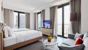 A hotel room with a bed, sofa, TV, and a city view. - Bomonti Suites (Istanbul)