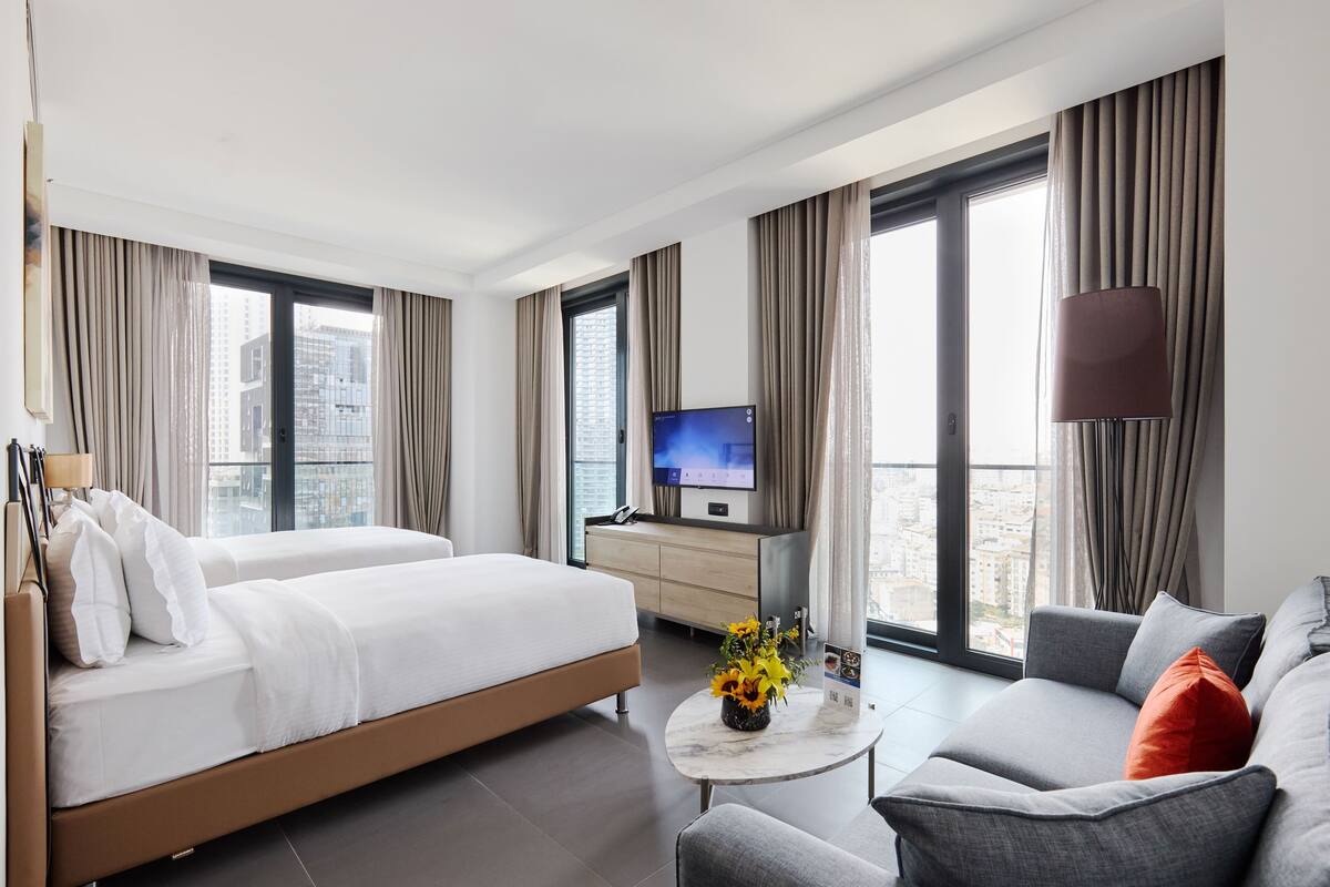 A hotel room with a bed, sofa, TV, and a city view.