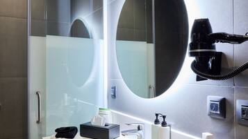 Ein modernes Badezimmer mit einer in Glas abgeschirmten Dusche, einem großen Spiegel und einem an der Wand befestigten Föhn.