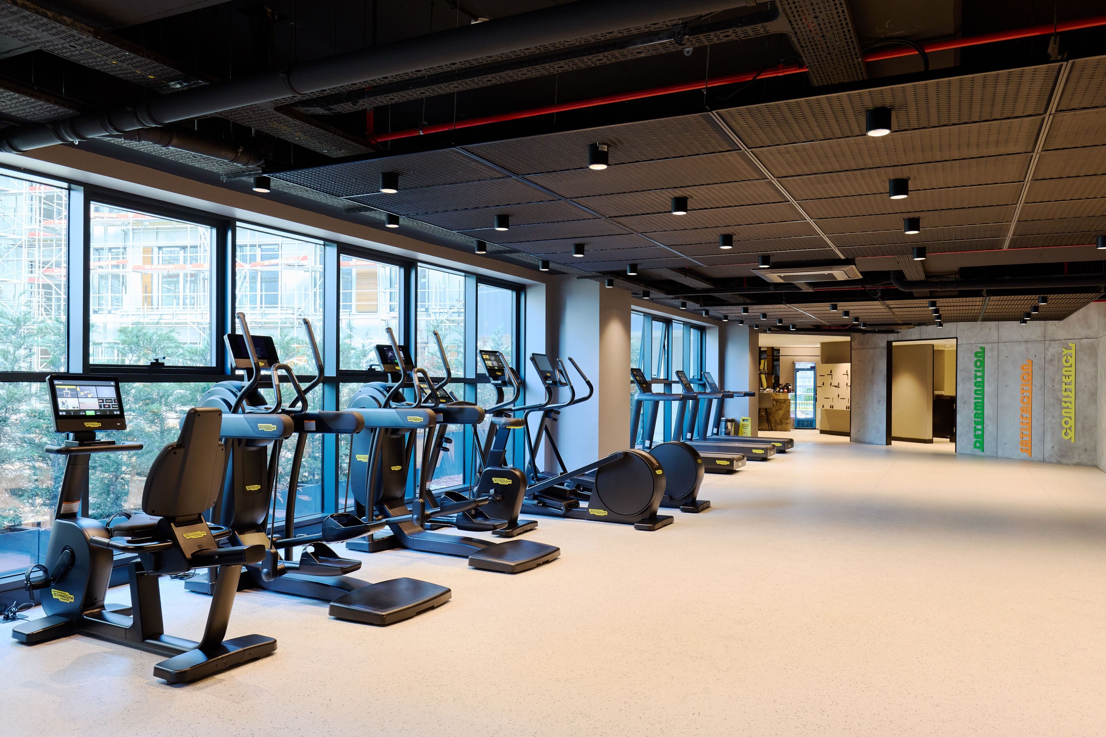 Een fitnessruimte met trainingsapparatuur, grote ramen en een schoon, modern interieur.