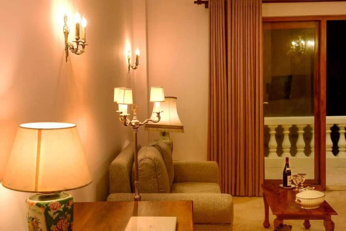 Uma sala de estar aconchegante com uma mesa de madeira, um sofá e uma poltrona. Há duas luminárias na parede e uma janela com cortinas.