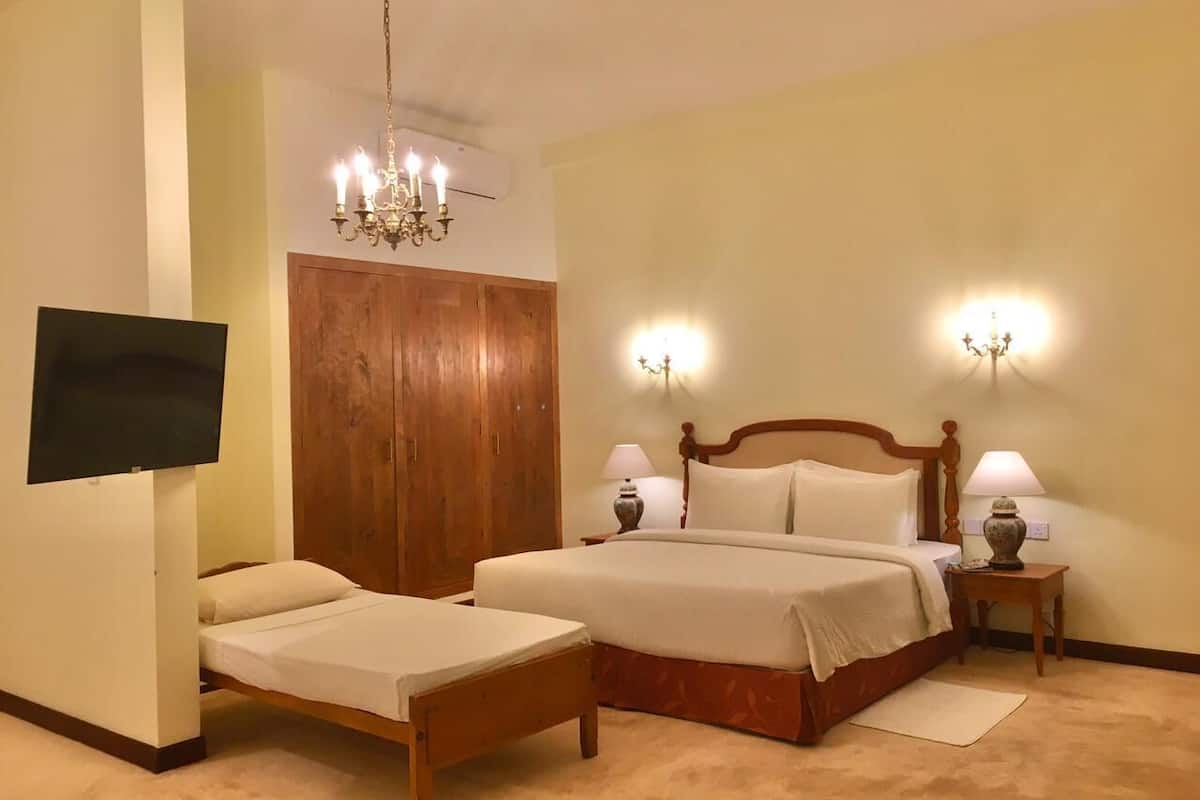 Quarto com cama grande, guarda-roupa de madeira, televisão na parede e duas luminárias de cabeceira.