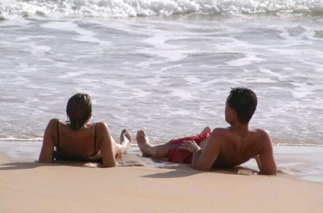 Dos personas descansando en la playa, con el océano al fondo.