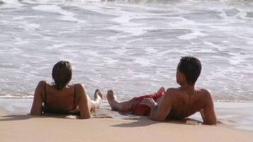 Dos personas descansando en la playa, con el océano al fondo.
