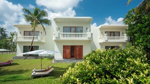 A two-story resort building with balconies, a pool area with lounge chairs, and lush greenery. - Samsara (Boossa)