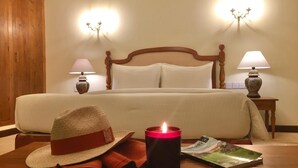 A hotel room with a bed, bedside lamps, a candle, a hat, and a magazine on the floor. - Samsara (Boossa)