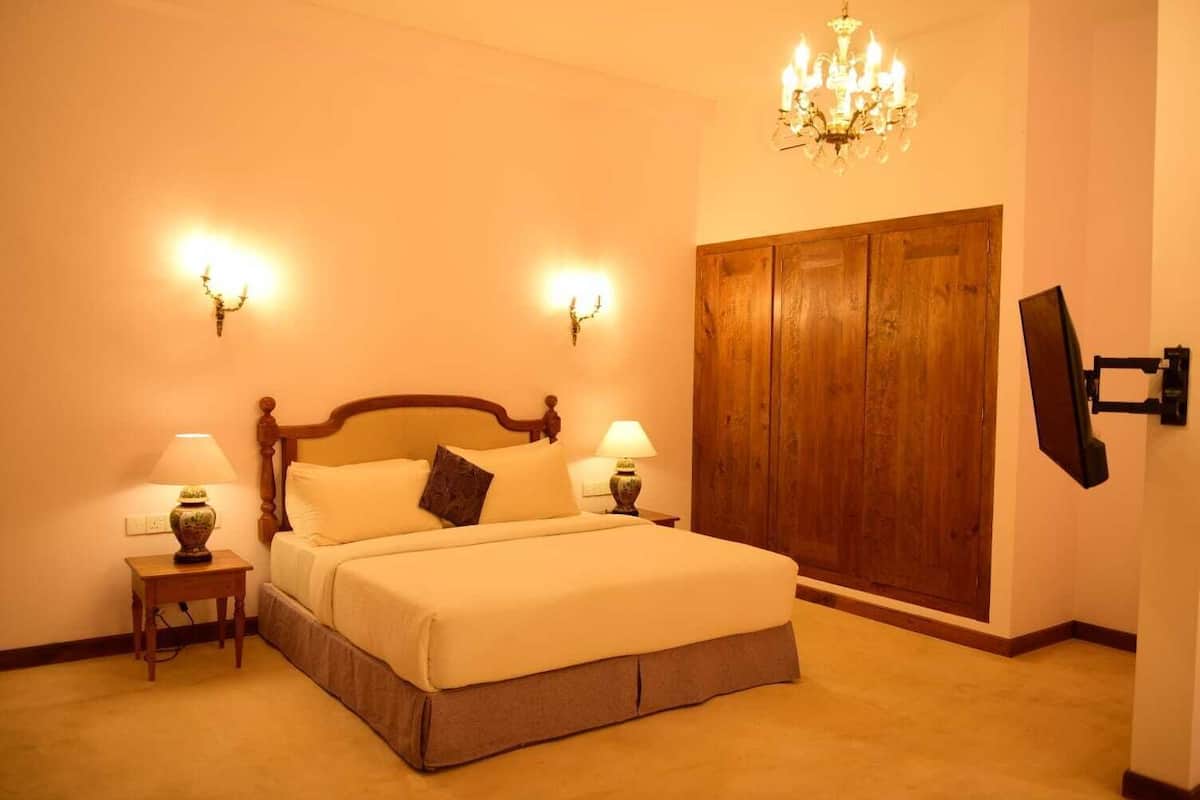 Quarto com uma cama grande, duas mesas de cabeceira com abajures, um guarda-roupa de madeira e um candelabro.