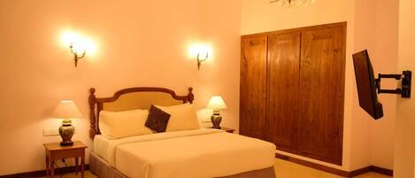 A bedroom with a large bed, two bedside tables with lamps, a wooden wardrobe, and a chandelier.