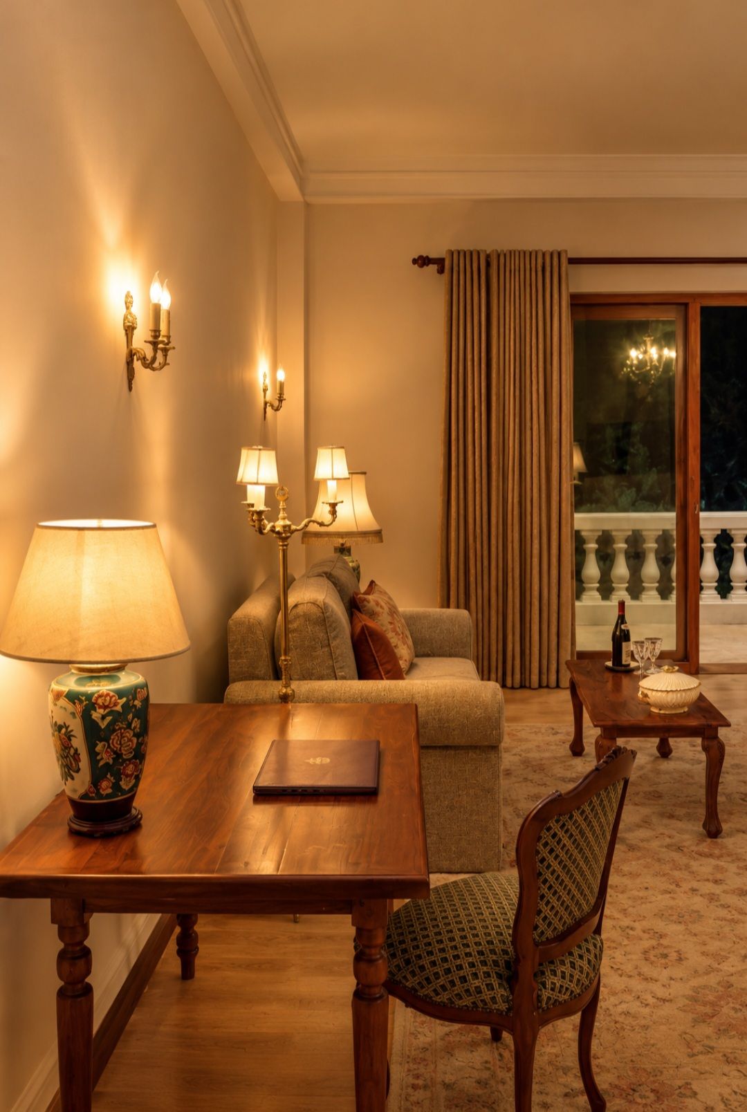 Una sala de estar acogedora con una mesa de madera, un sofá y un sillón estampado. Hay apliques y una lámpara de pie que proporcionan iluminación ambiental.