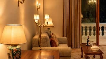 Una sala de estar acogedora con una mesa de madera, un sofá y un sillón estampado. Hay apliques y una lámpara de pie que proporcionan iluminación ambiental.