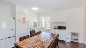 Une cuisine moderne avec des meubles blancs, une table à manger en bois et un four encastré.
