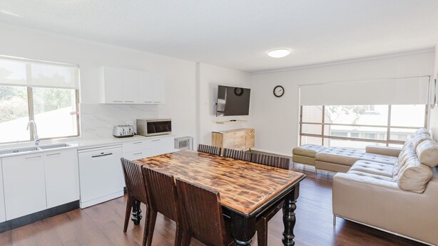 Une cuisine moderne avec des meubles blancs, une table à manger en bois et un four encastré.