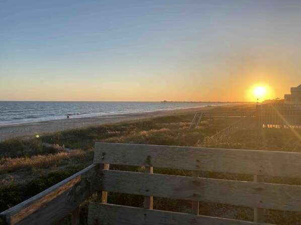 Un banco de madera con vistas a una playa y un atardecer de fondo.