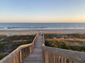 Un paseo marítimo de madera que conduce a una playa, con el océano al fondo.
