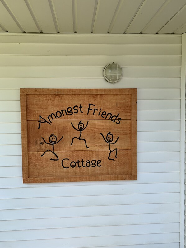 A wooden sign with stick figures and the text "Amongst Friends Cottage" on a white wall. - Amongst Friends Cottage (Pelee Island)