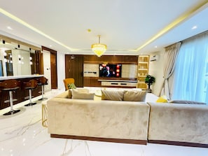 A modern living room with a large sofa, a TV, a chandelier, and a bar area.