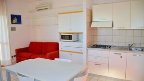 A compact kitchen with white cabinets, a red sofa, a dining table, and a microwave.